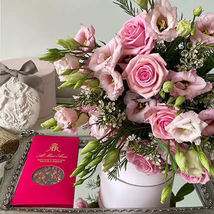 Ziedu pušķis rozā toņos no rozēm, lizantēm un dekoratīviem smalkziediem un piena šokolāde