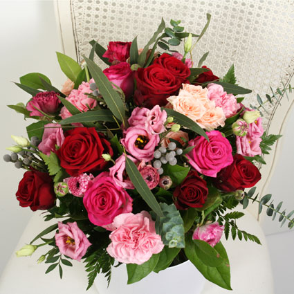 Flowers on-line. Flower bouquet of red and pink roses, pink lisianthus and pink carnations with decorative seasonal foliage.
