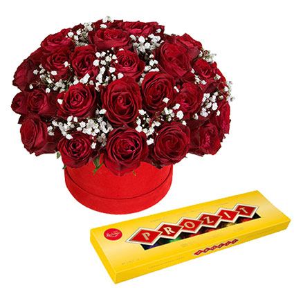The arrangement of red roses with white delicate gipsophila in a decorative flower box and chocolates