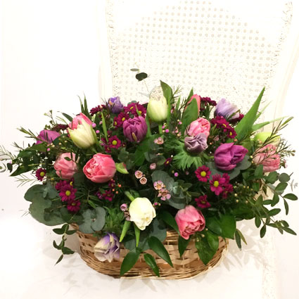 Flower delivery Riga. Flower basket with multicolored tulips, anemones, and decorative seasonal foliage.